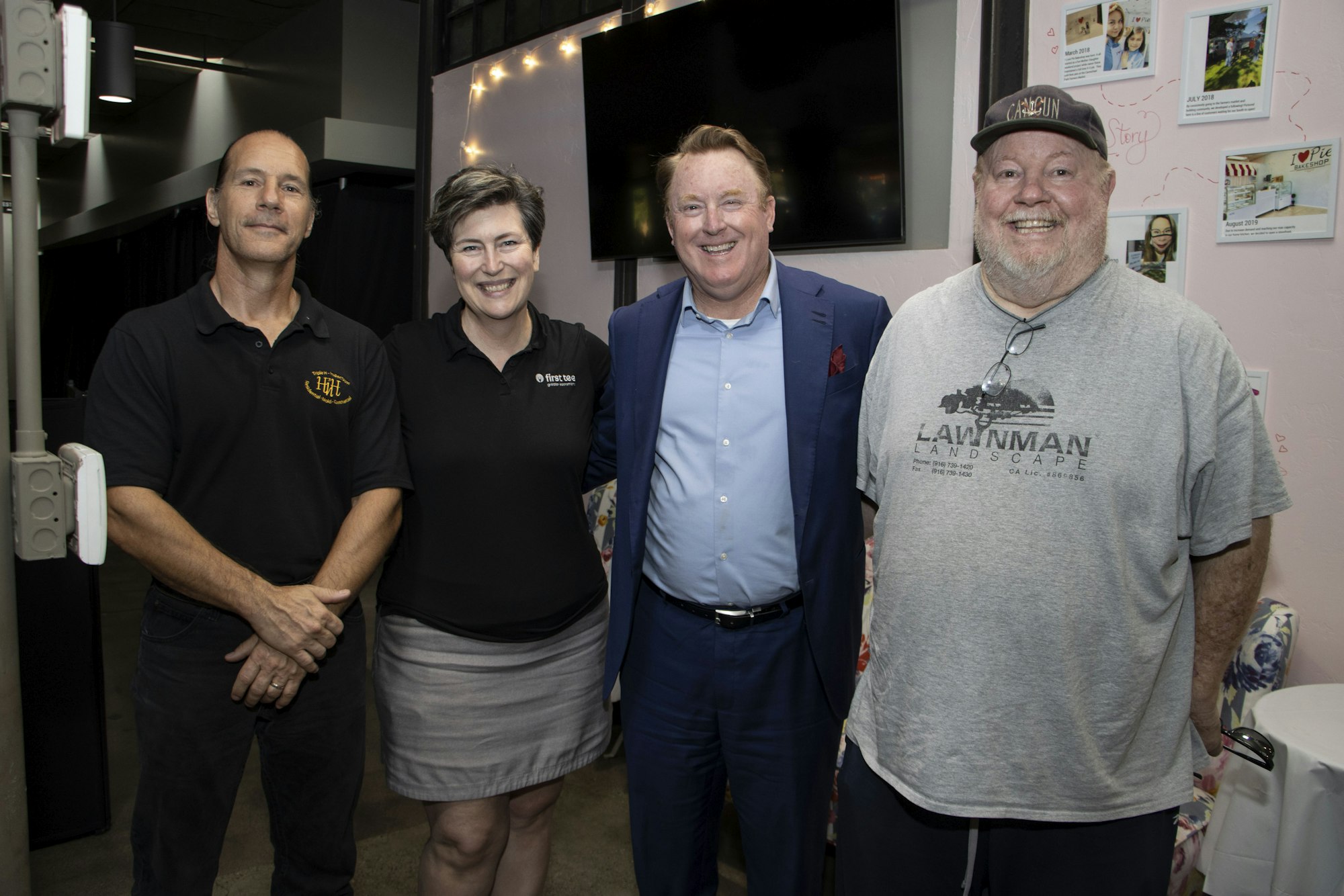 Four people smiling for a group photo indoors, one in a suit, others in casual attire.