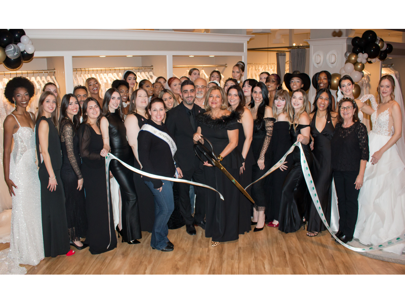 A group of people at a ribbon-cutting ceremony, with scissors and dresses displayed in the background.