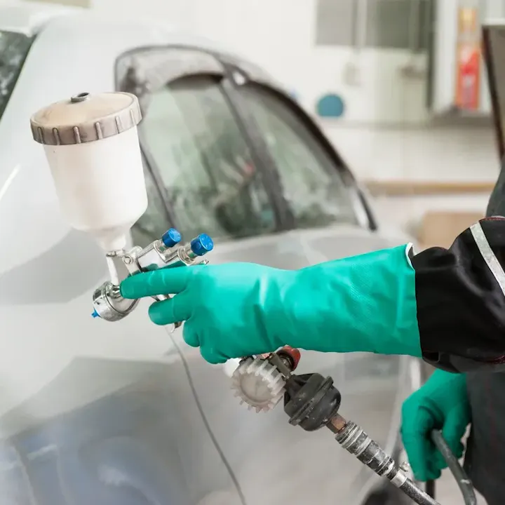 Person in gloves using spray gun to paint a car.