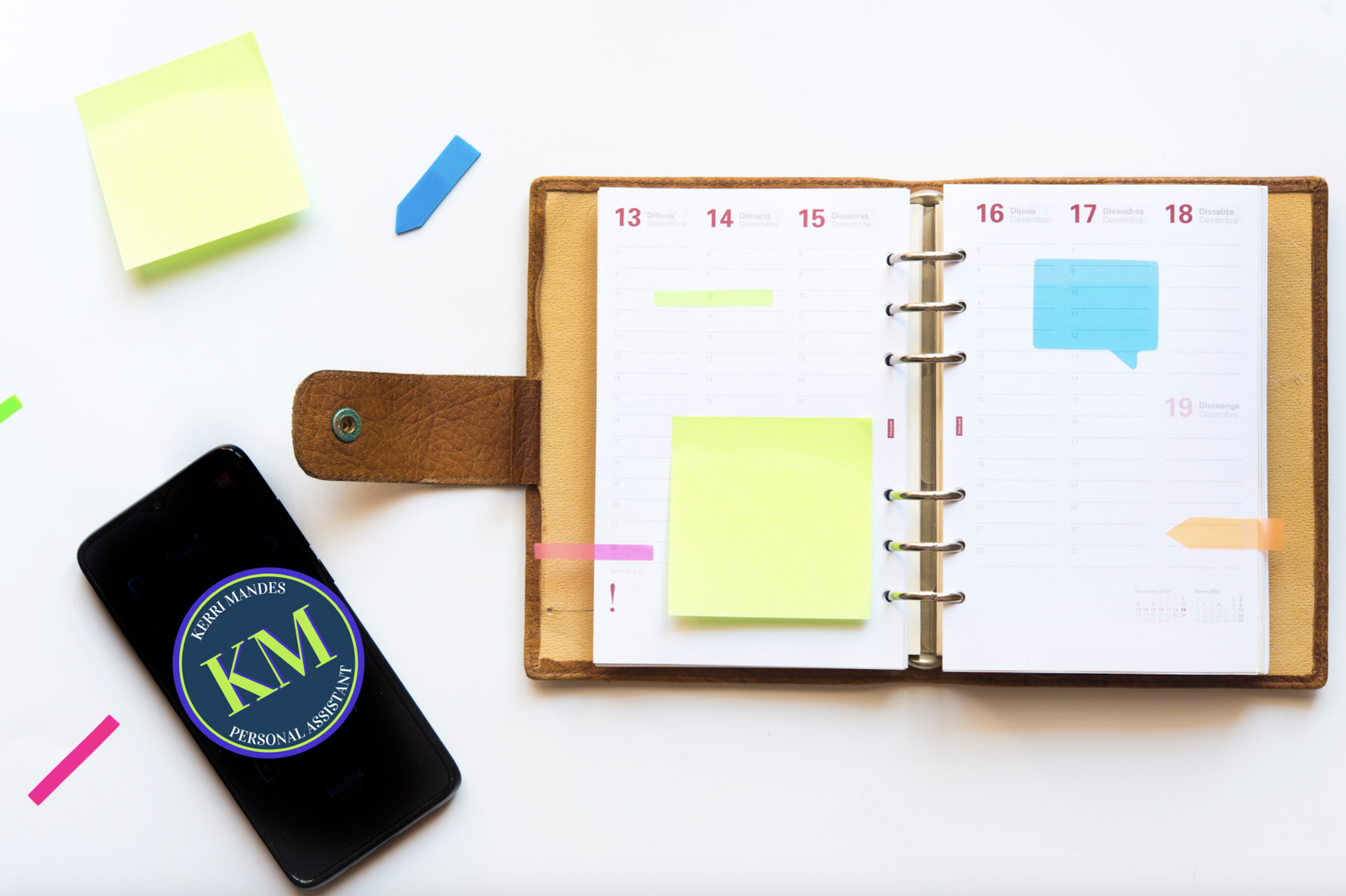 Open planner with sticky notes, smartphone with logo, colorful tabs on white background.