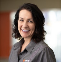 A person smiling and wearing a gray shirt with a blurred background.