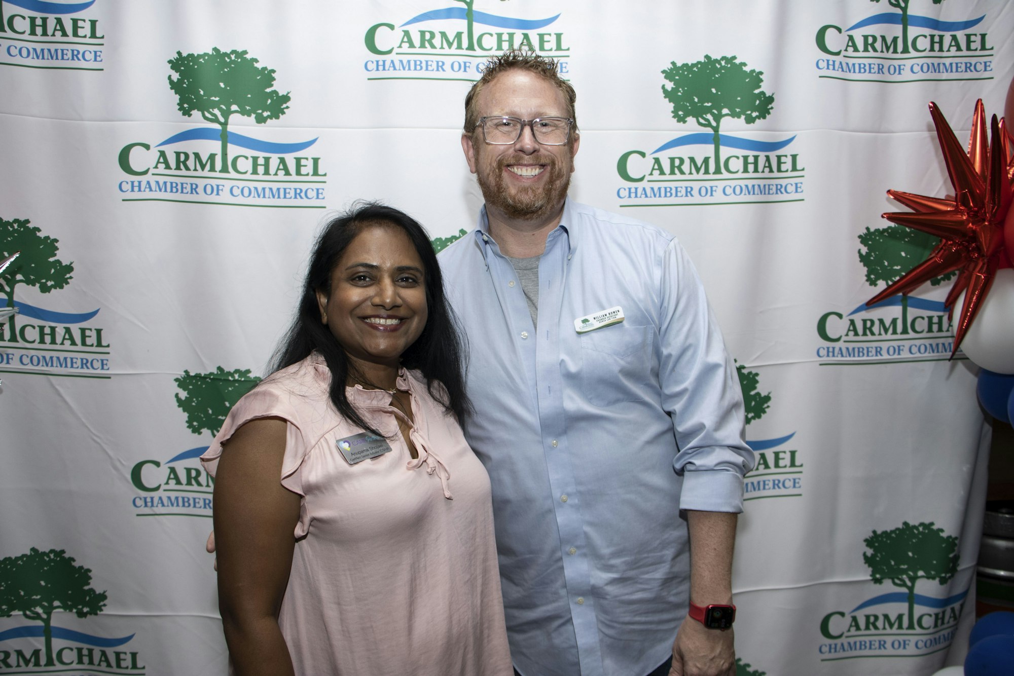 Two people smiling at a Carmichael Chamber of Commerce event backdrop.