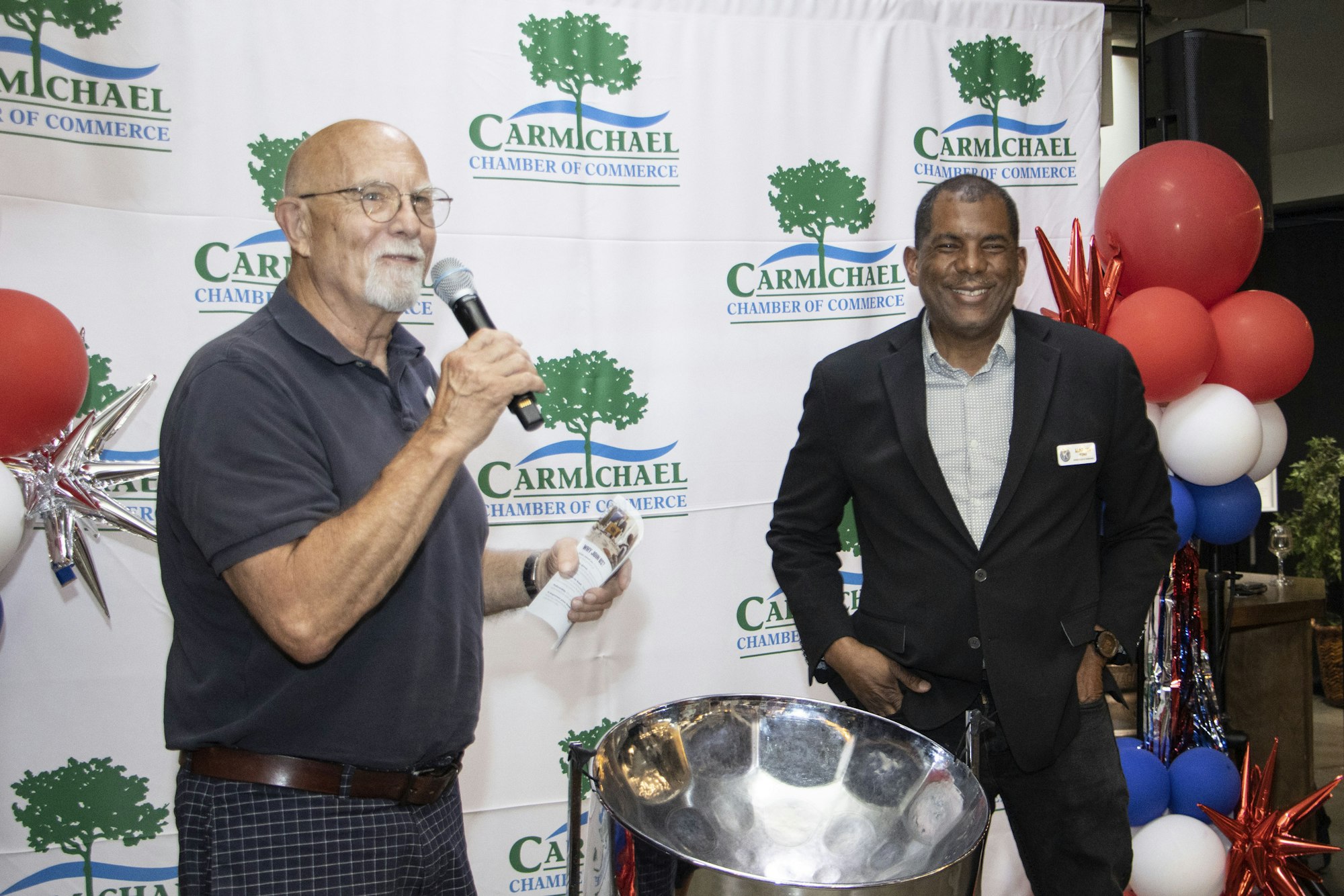 Two people at a Carmichael Chamber of Commerce event with balloons and logos in the background.