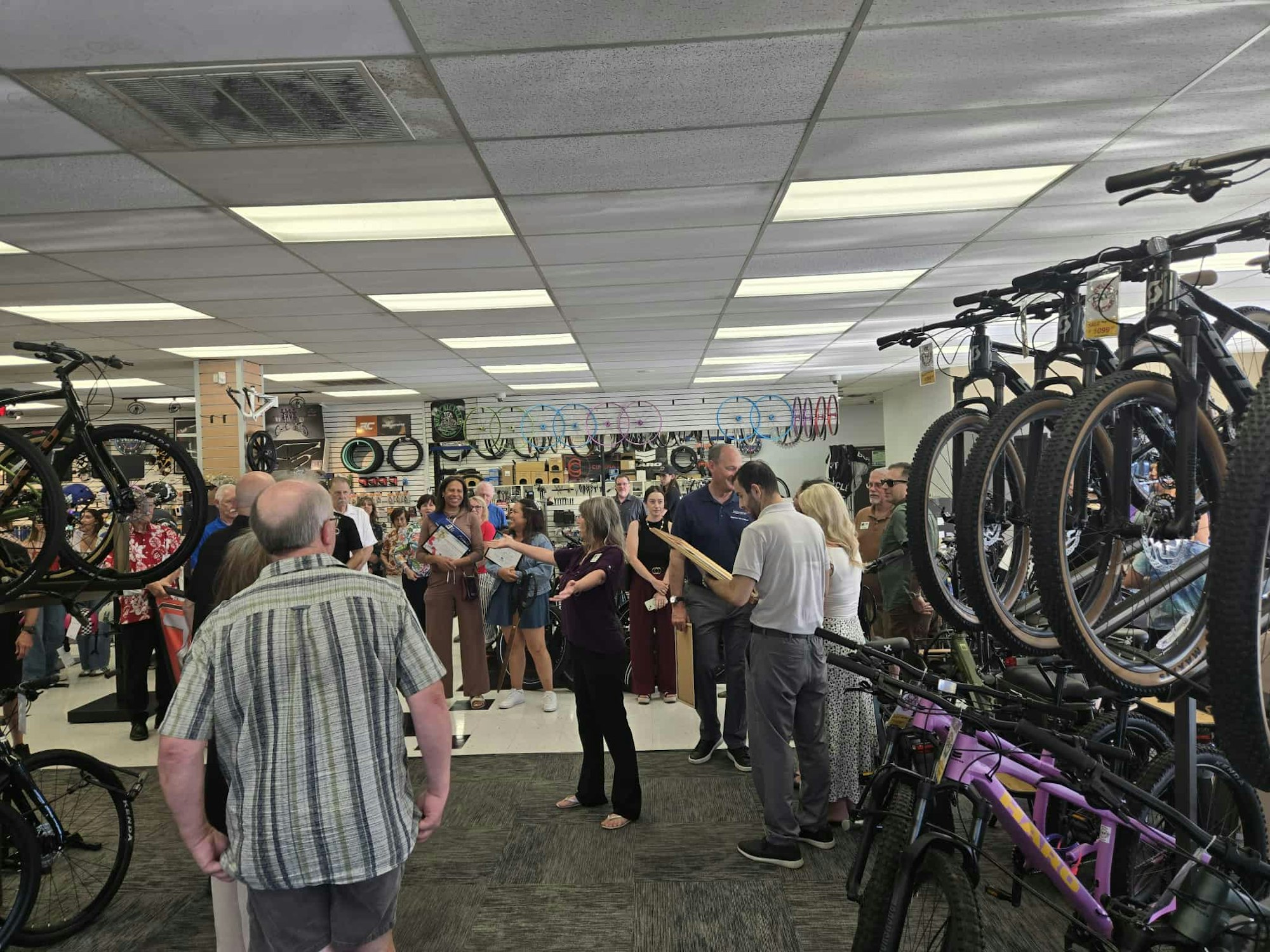 A group of people gathered in a bike shop, surrounded by bicycles and bike accessories.
