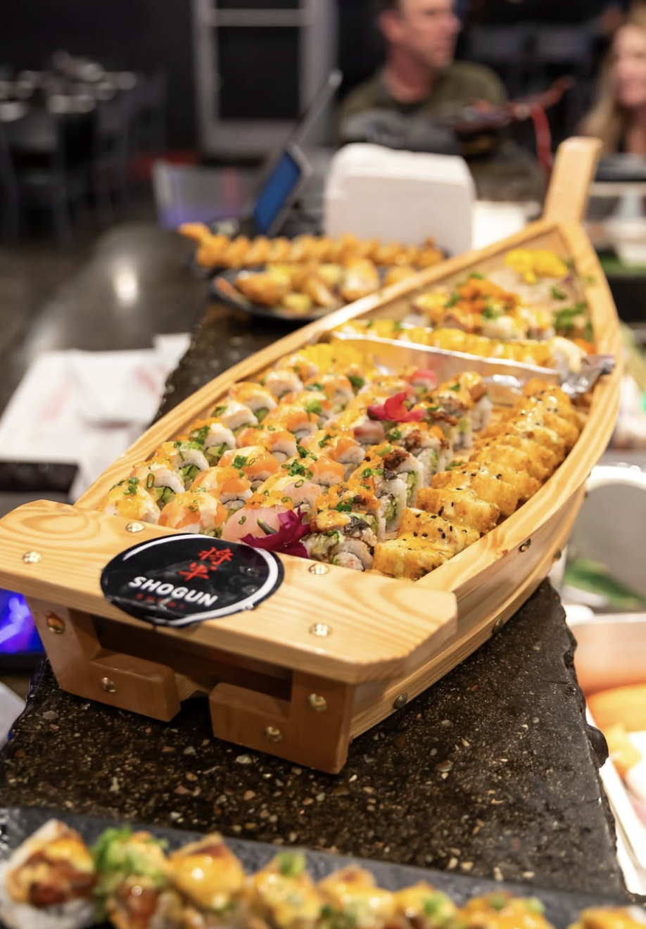 A boat-shaped platter filled with assorted sushi rolls, garnished and displayed on a table.