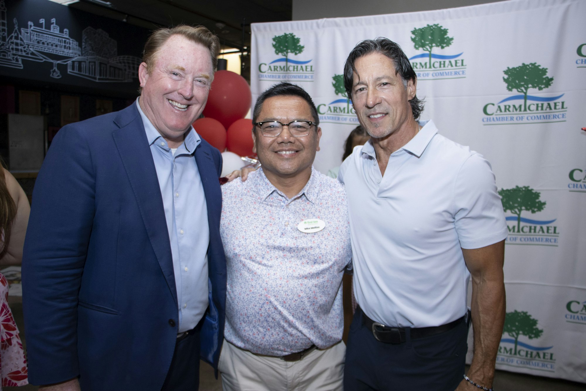 Three men posing together at a Carmichael Chamber of Commerce event, with balloons and a branded backdrop.