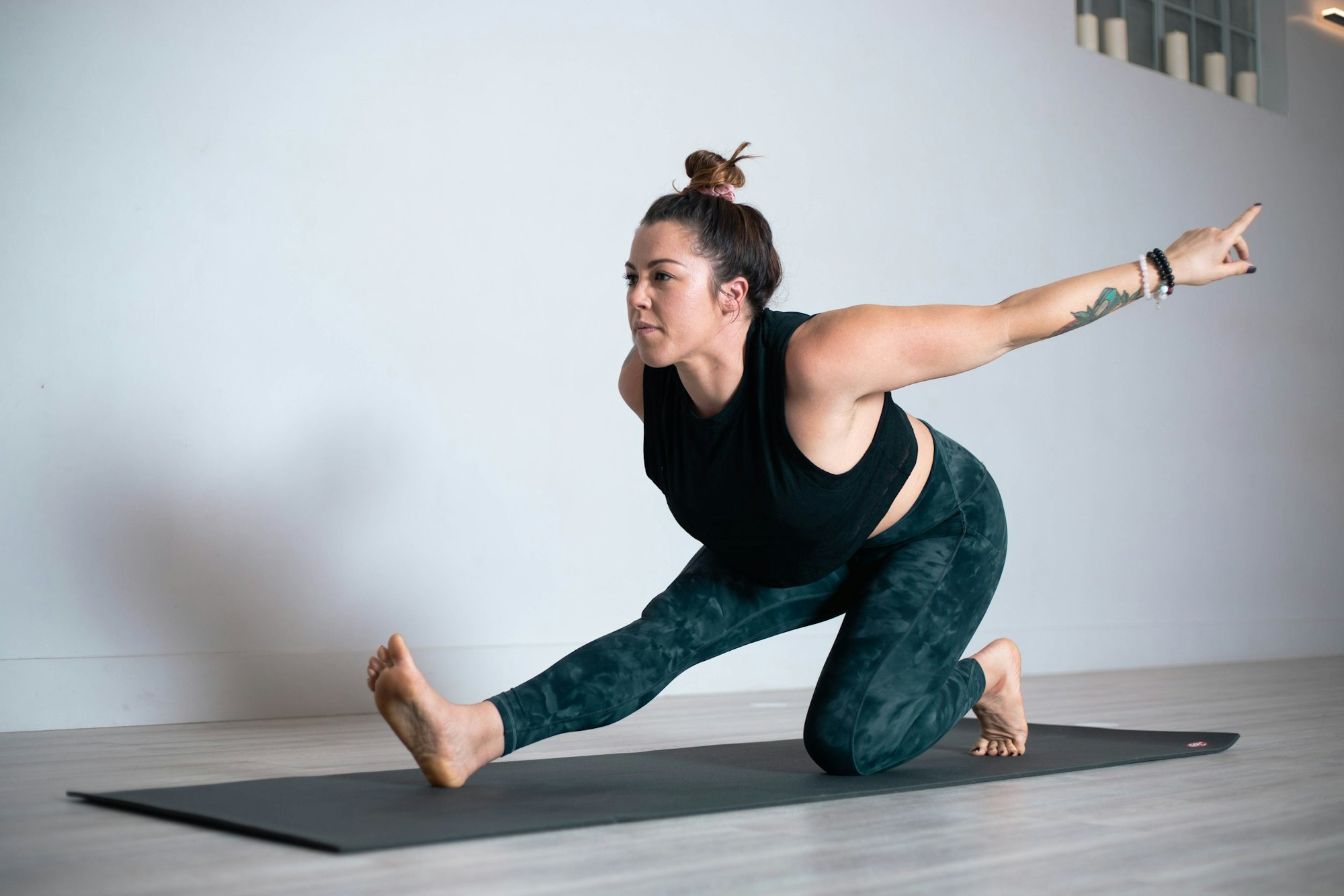 A person doing a yoga pose on a mat, one knee bent, with one arm extended, in a minimal indoor setting.