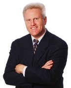 A person in a suit with crossed arms, smiling at the camera.