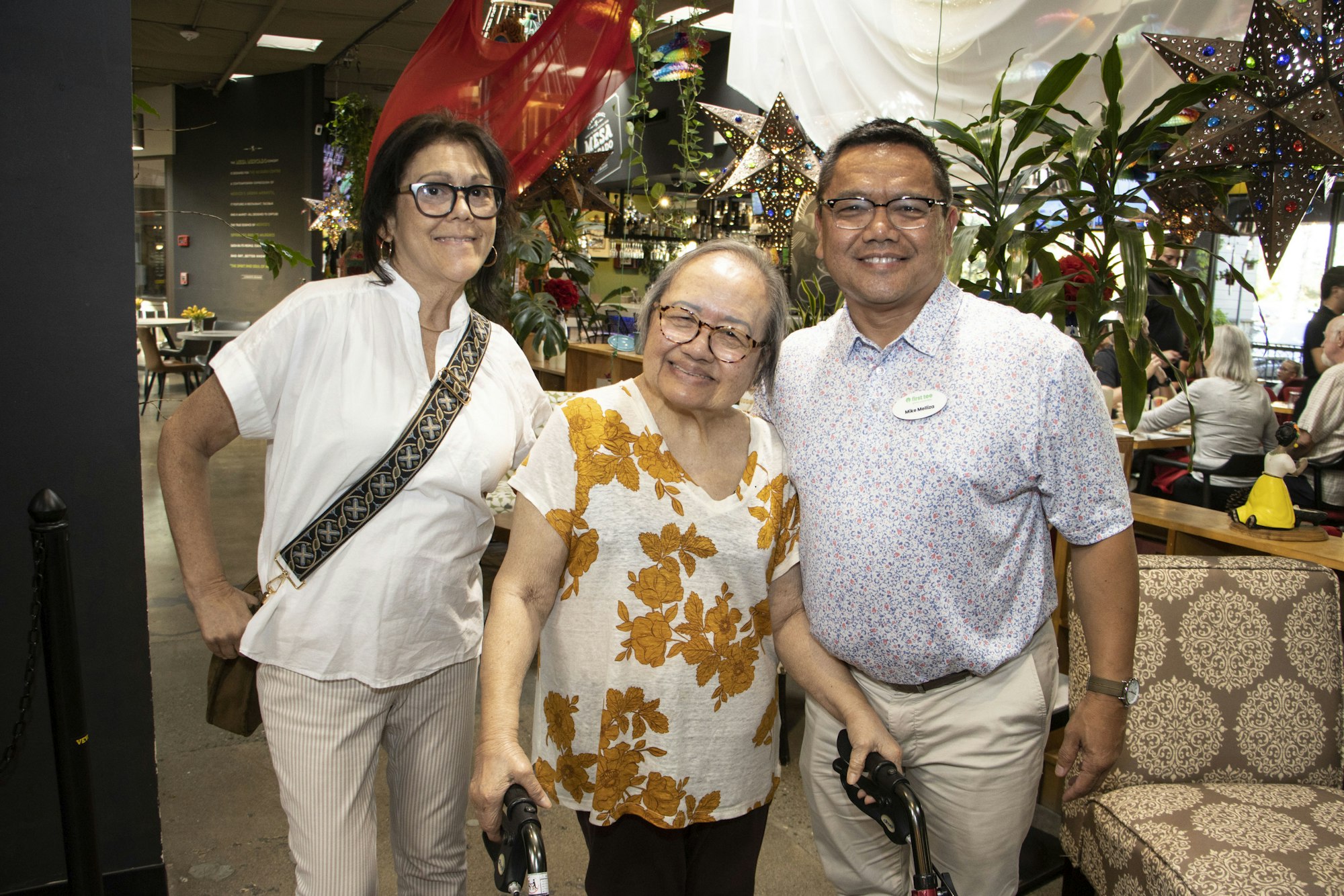 Three people smiling in a decorated room with plants and star ornaments.