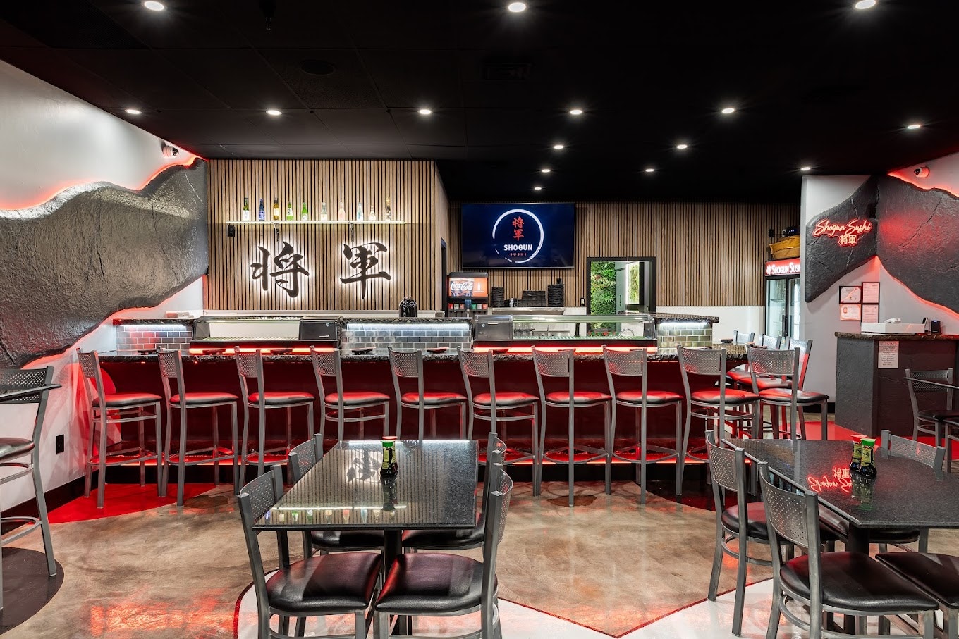 A sushi bar with red chairs, modern decor, and a "Shogun" sign above a counter with bottles and a TV screen.