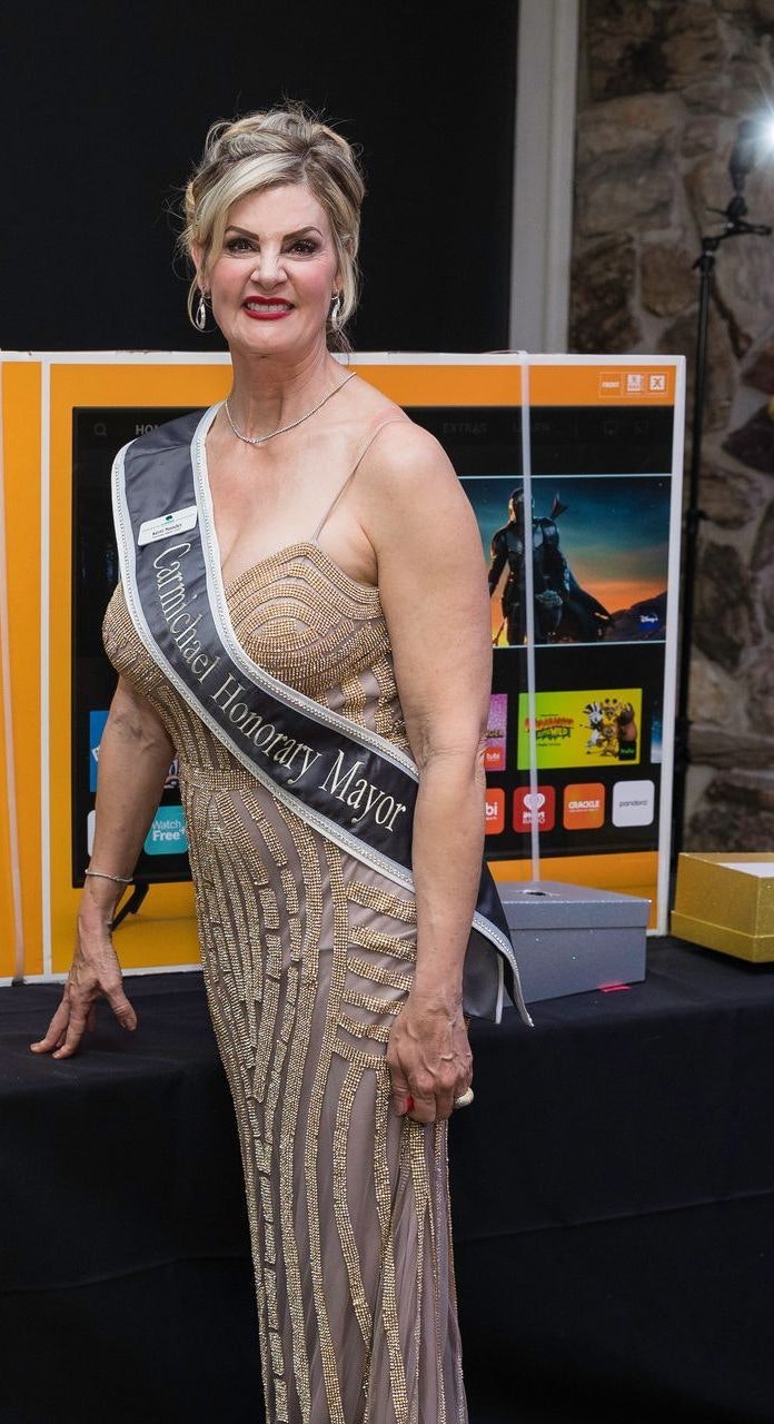 A person wearing a sash that reads "Carmichael Honorary Mayor," smiling at a formal event.