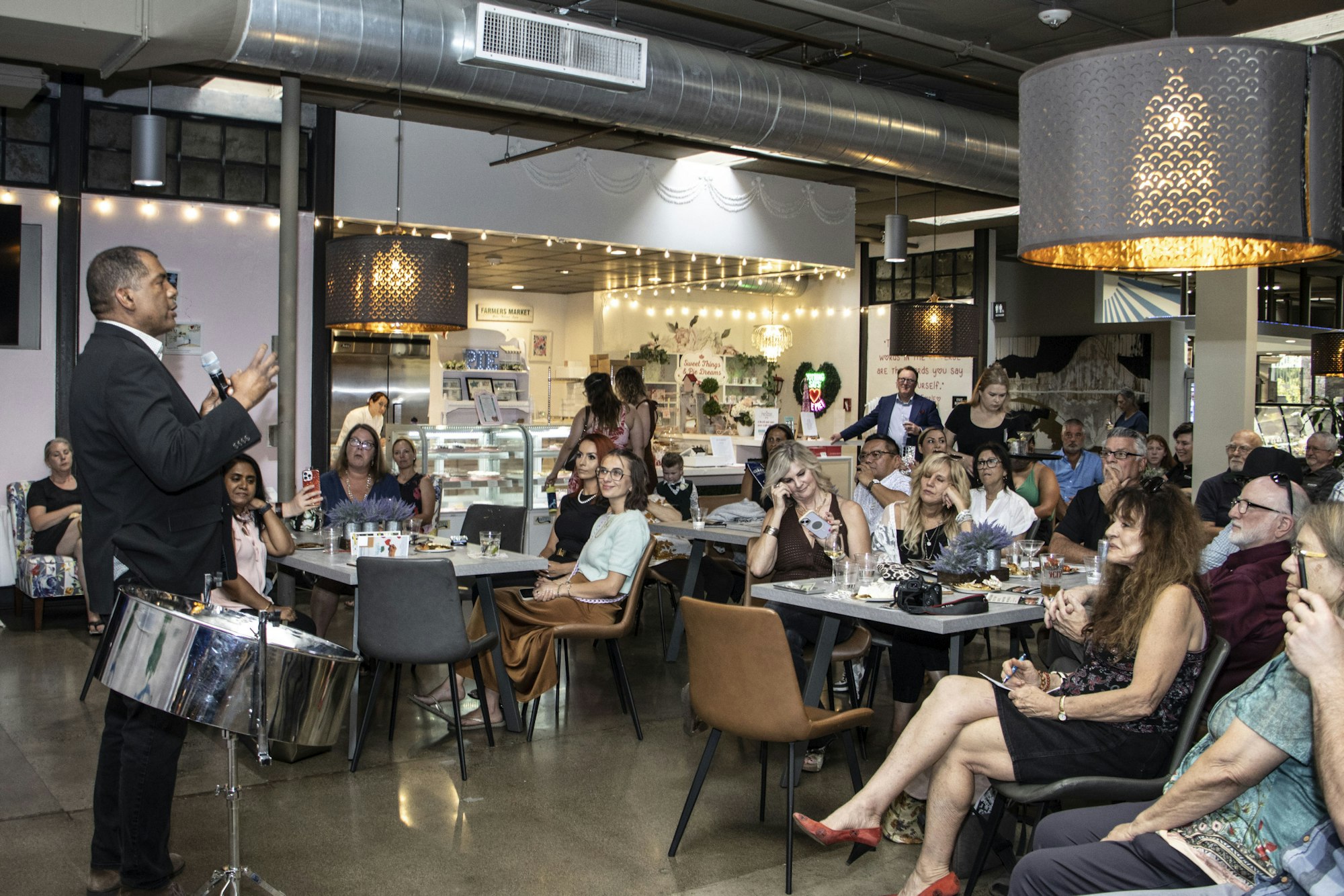 A speaker engages an audience in a modern, well-lit venue with tables and decorations.