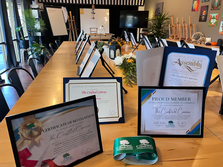 The image shows a table set with awards and certificates for "The Crafted Canvas," highlighting recognition and membership.