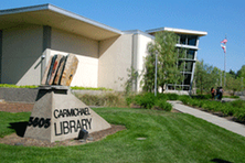 A library building with a sign and green lawn under a clear sky.