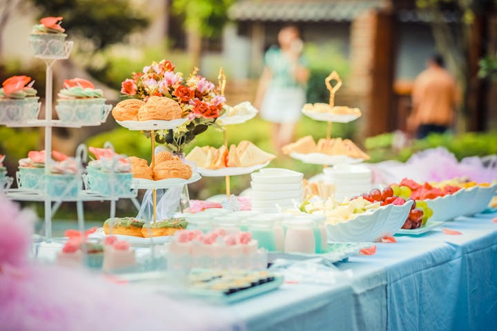 A table set with pastries, fruit, sandwiches, cupcakes, and drinks, adorned with flowers.