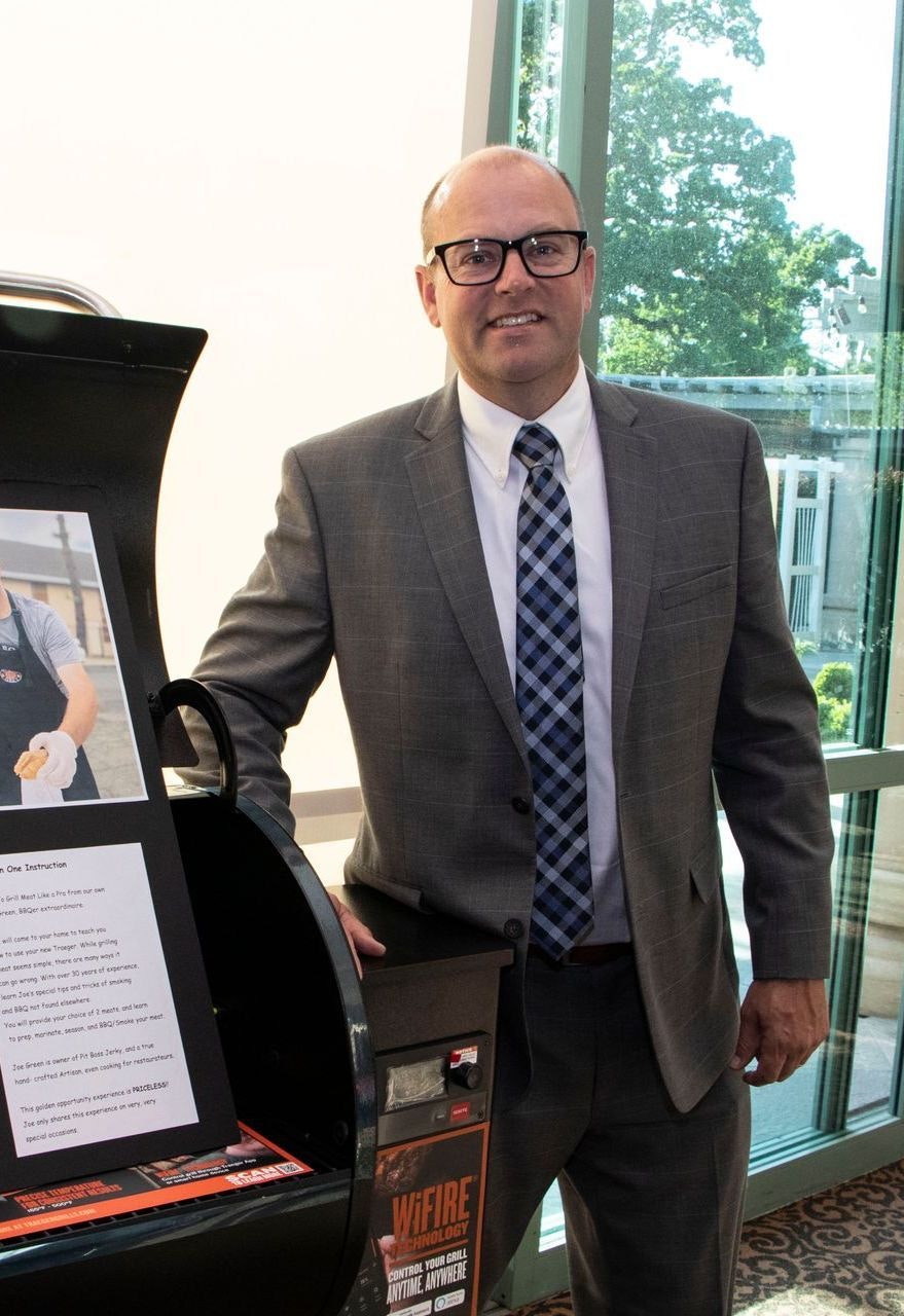 A smiling man in a suit standing next to a display with text and pictures.