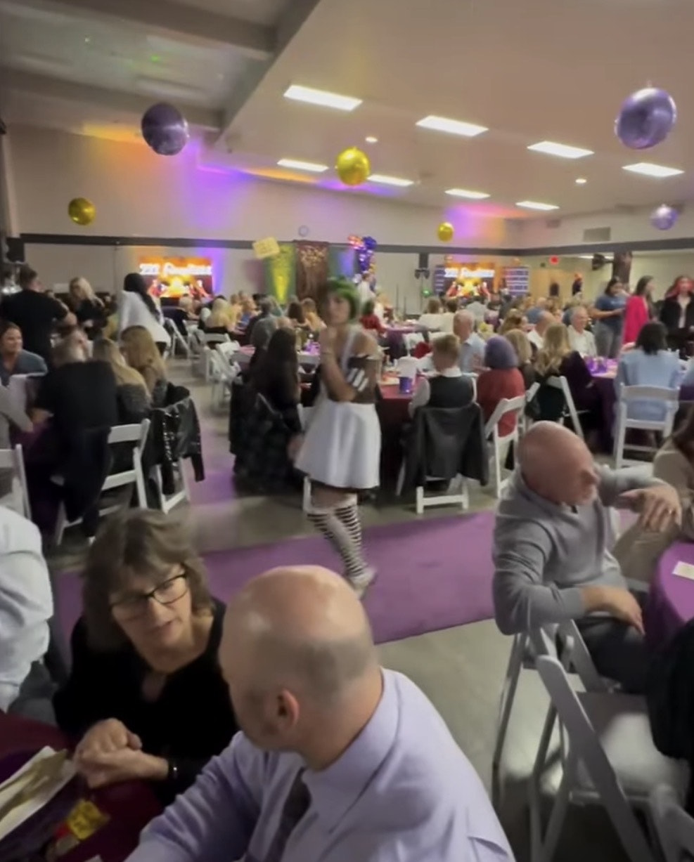 A festive indoor gathering with people seated at tables, colorful lights, and decorations in a hall setting.