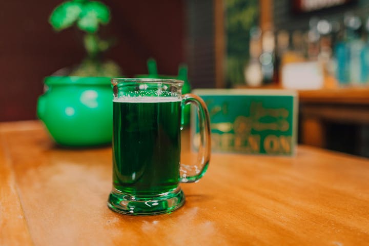 A mug of green liquid on a wooden table with a green pot in the background.