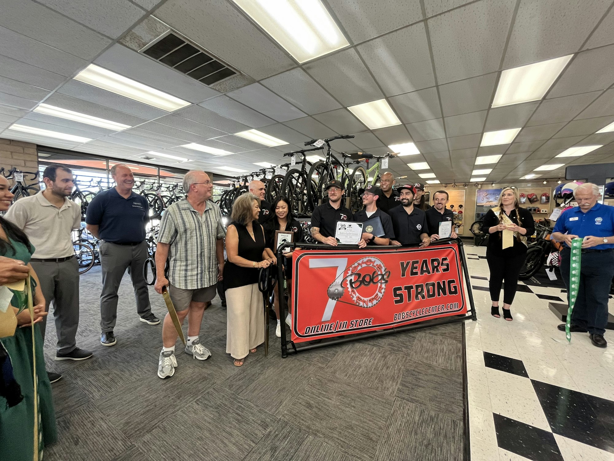 A group of people standing in a bike shop, holding a banner celebrating "70 Years Strong" for Bob's Cycle Center.
