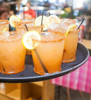 A tray of drinks with ice, garnished with lemon slices, served in clear cups with straws.