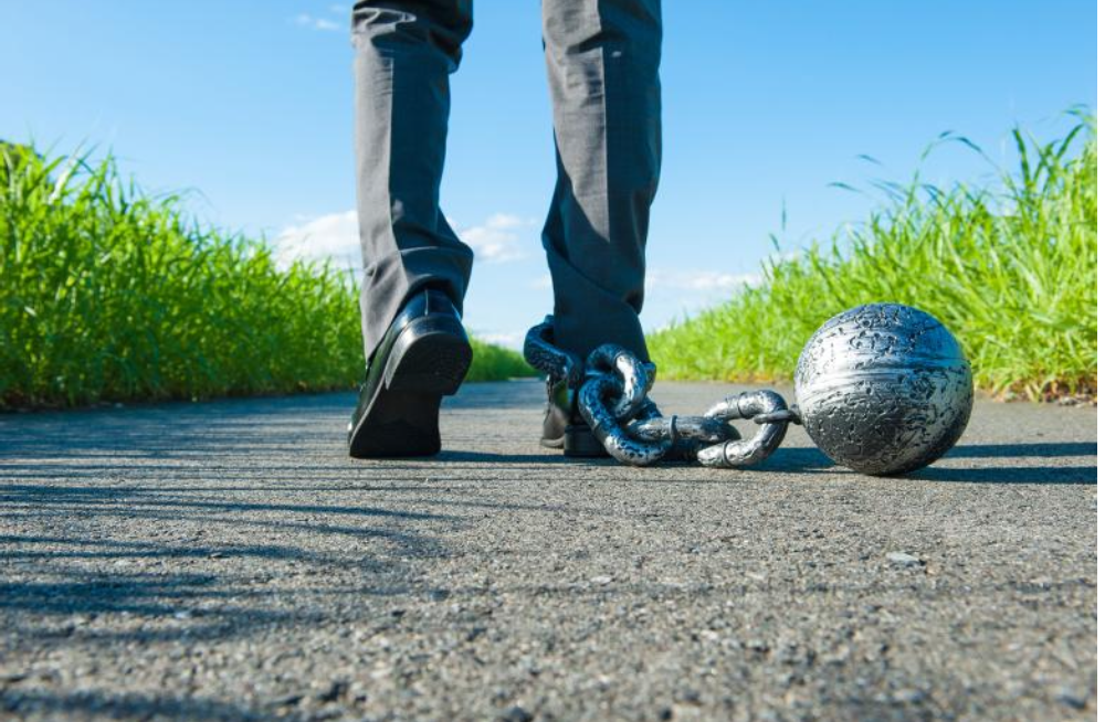 A person walking on a path with a ball and chain attached to the ankle, surrounded by green grass.