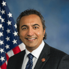Person smiling in a suit with an American flag background.