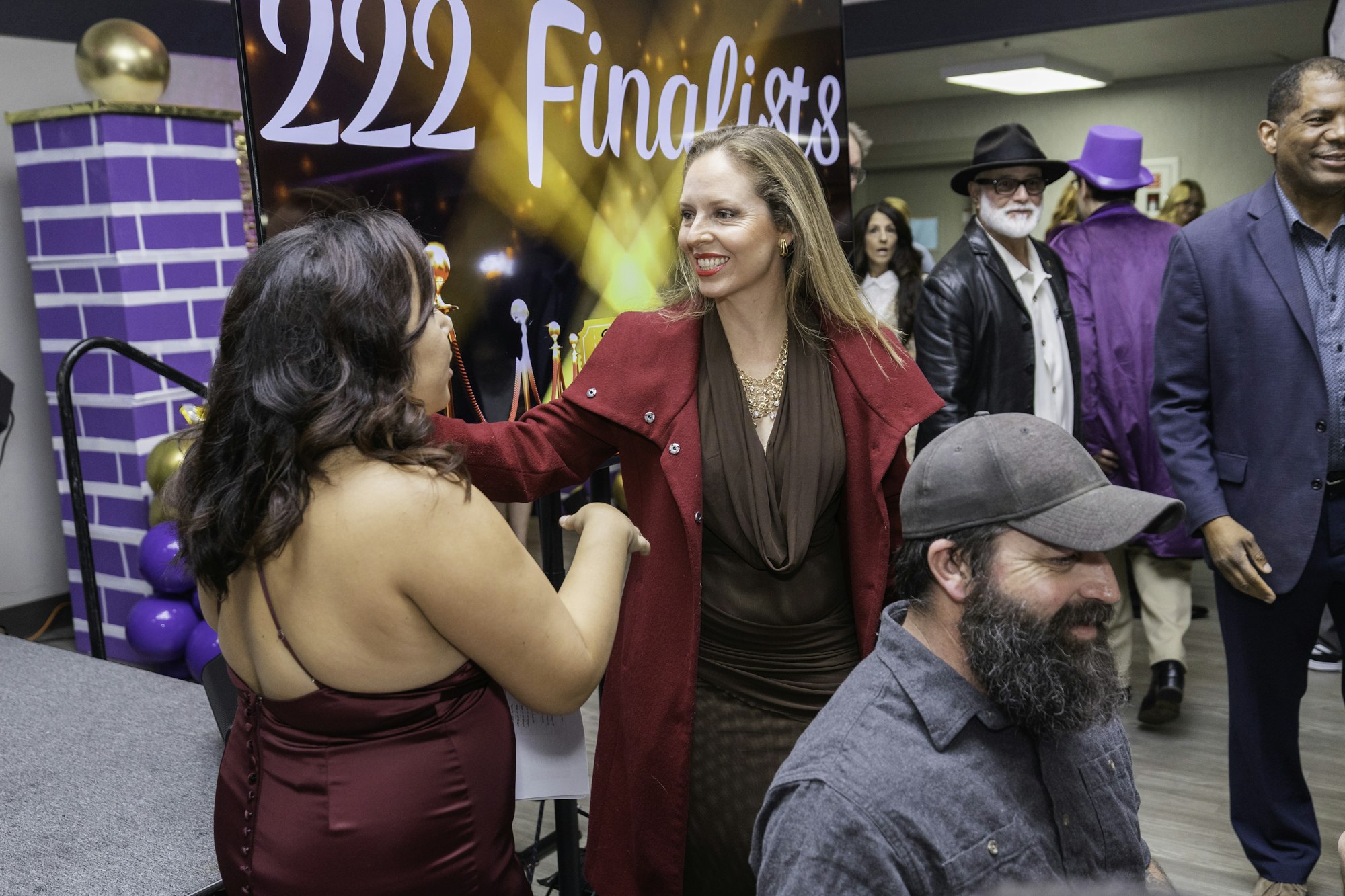 People at an event with a "222 Finalists" sign. Two women are shaking hands, others are in the background.