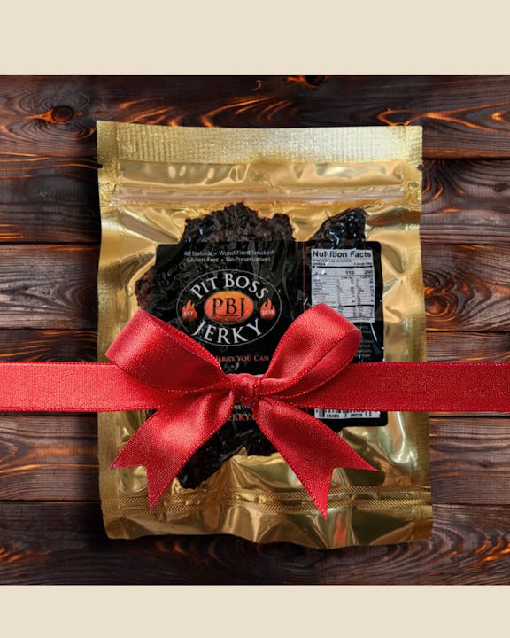 The image shows a package of Pit Boss PBJ jerky, decorated with a red ribbon, on a wooden background.