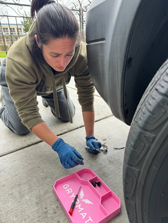 Person working on a car with tools and a pink tray on the ground.
