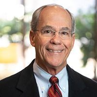 A smiling person in a suit with a red tie and glasses.