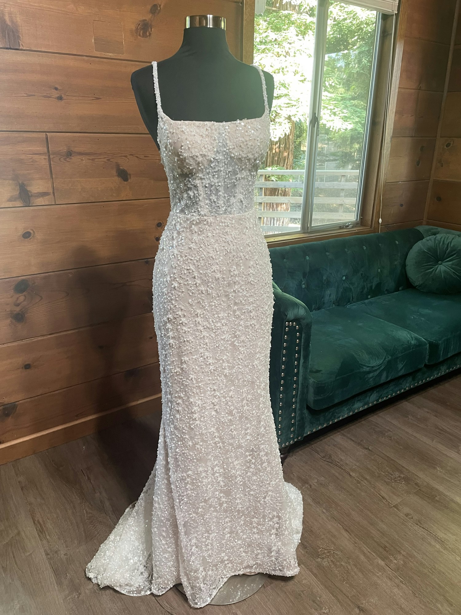 A sequined dress on a mannequin in a wooden room with a window and green sofa.