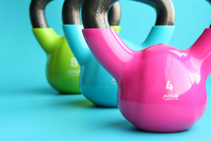 Three colorful kettlebells: pink, blue, green, on a turquoise background.