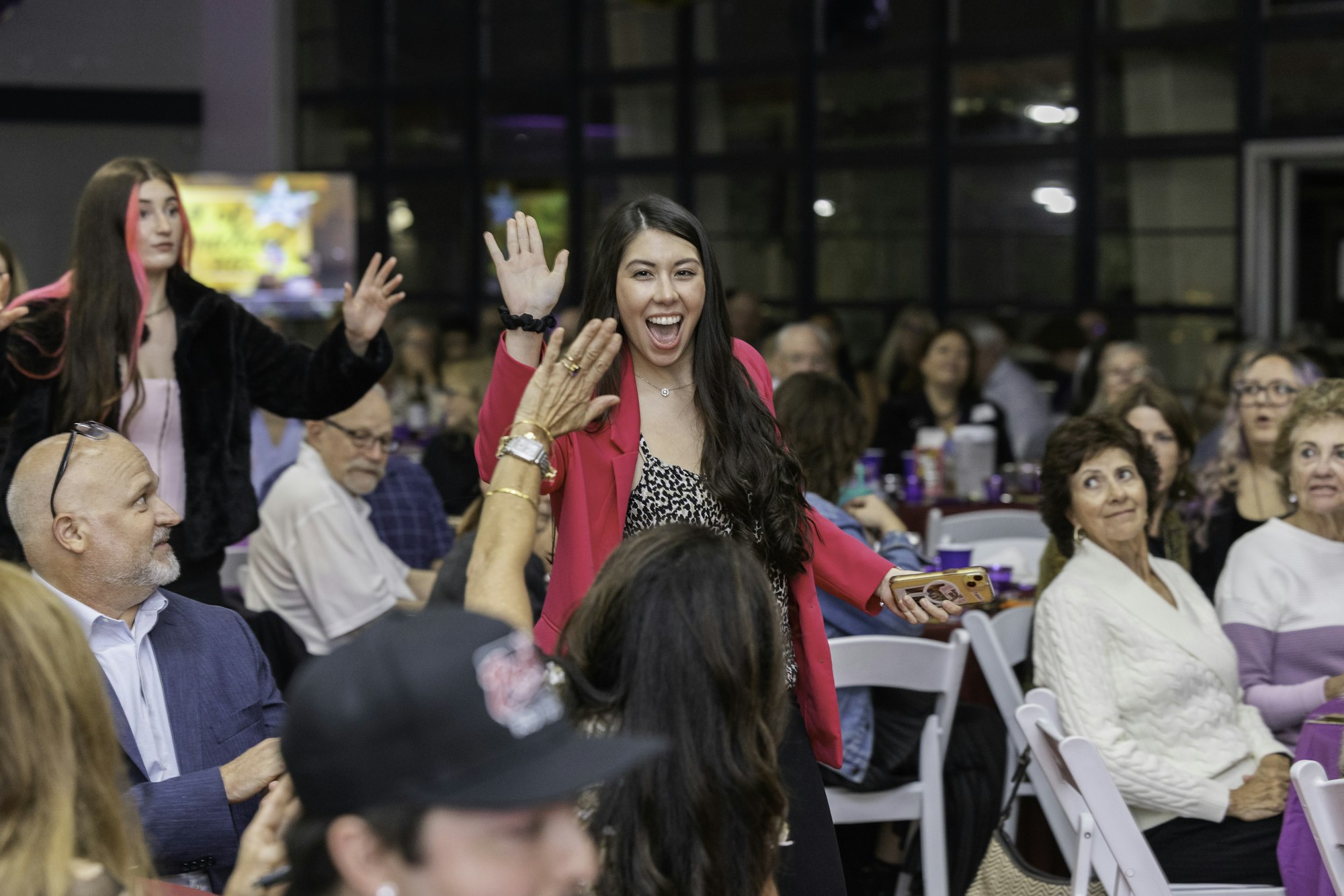A woman in a pink jacket enthusiastically high-fives in a crowded indoor event.