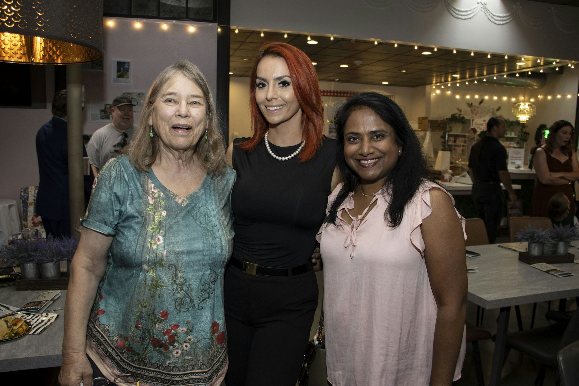 Three women smiling and posing together in a festive indoor setting.