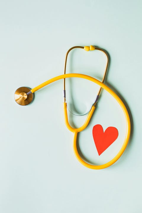 A yellow stethoscope next to a red paper heart on a light background.