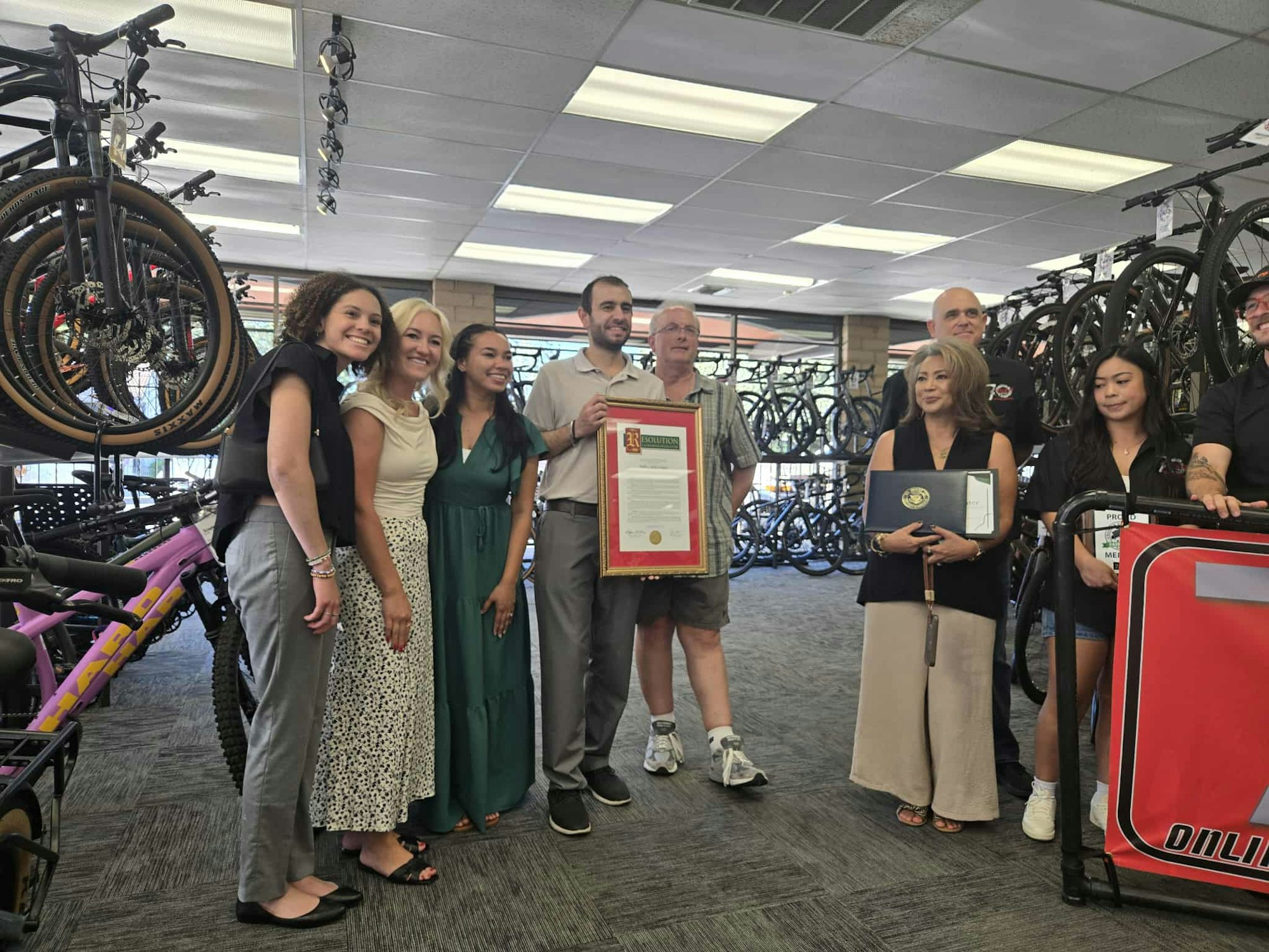 A group of people in a bike shop, with some holding certificates and standing near bicycles.