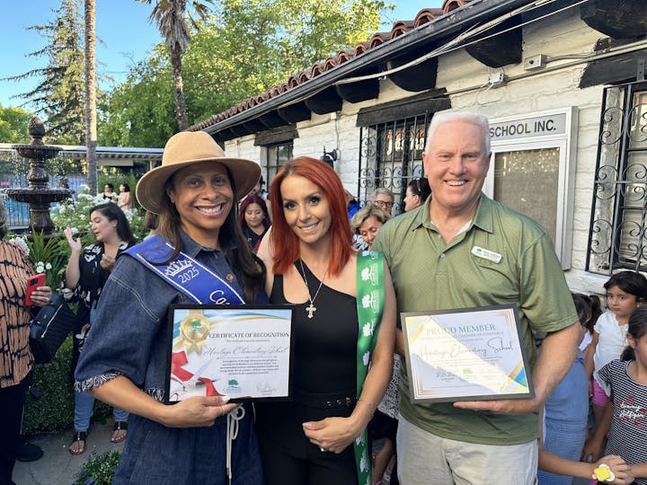 Three people smiling, holding certificates, with a crowd in the background.
