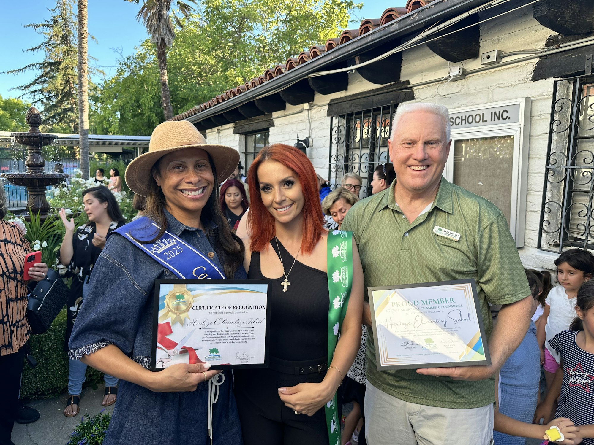 Three people smiling, holding certificates, with a crowd in the background.