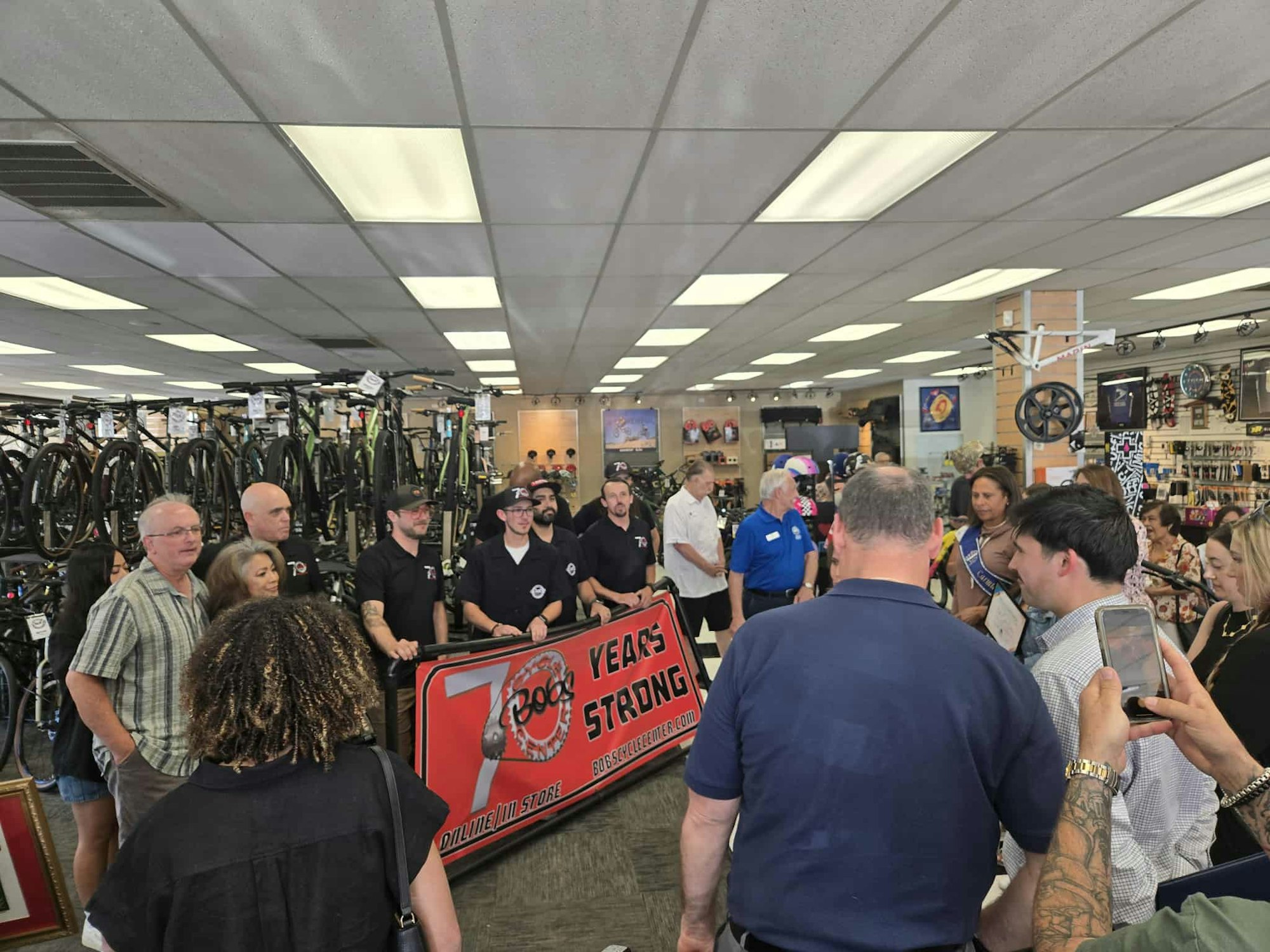 A group of people gathered in a bicycle store, holding a banner celebrating 70 years.
