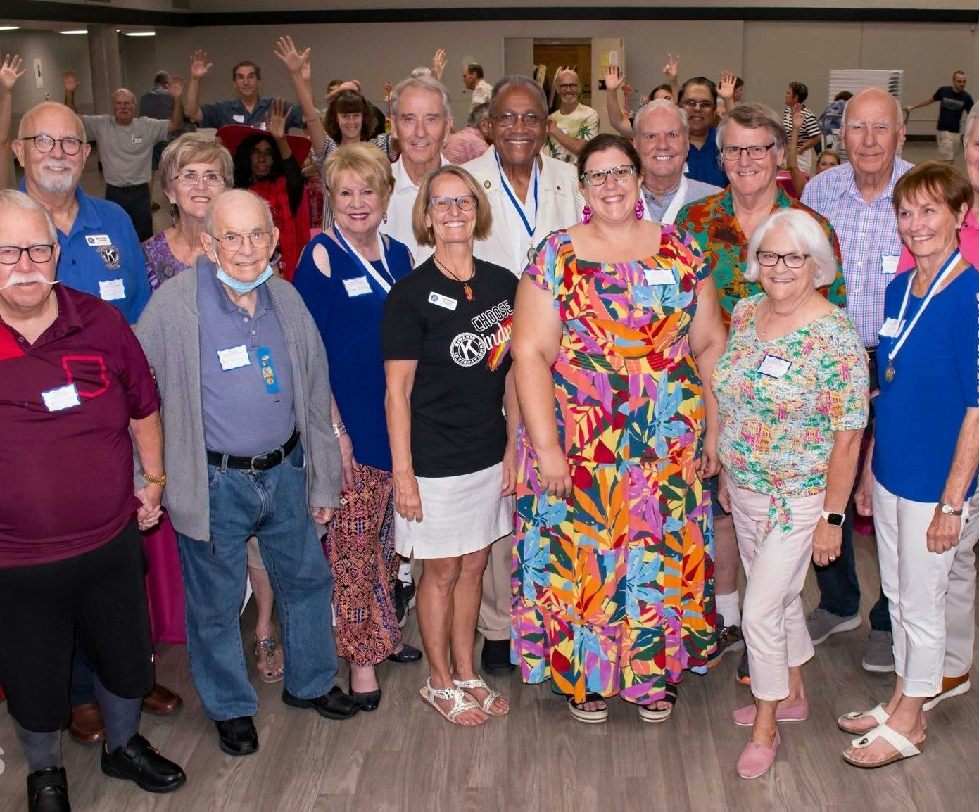 A group of smiling people posing for a photo, some wearing name tags and waving.