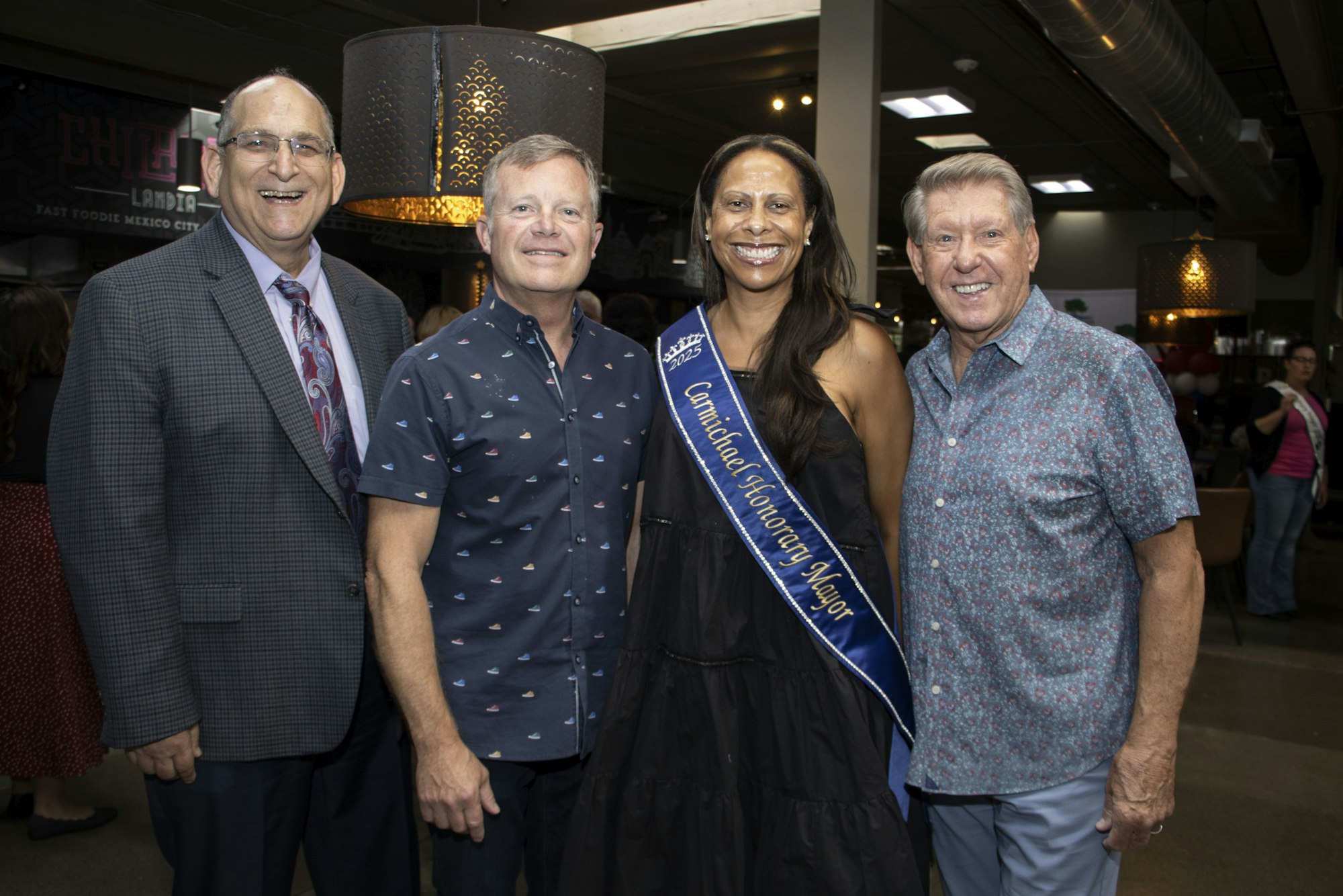 Four people posing together; one wearing a sash that reads "Carmichael Honorary Mayor 2023".
