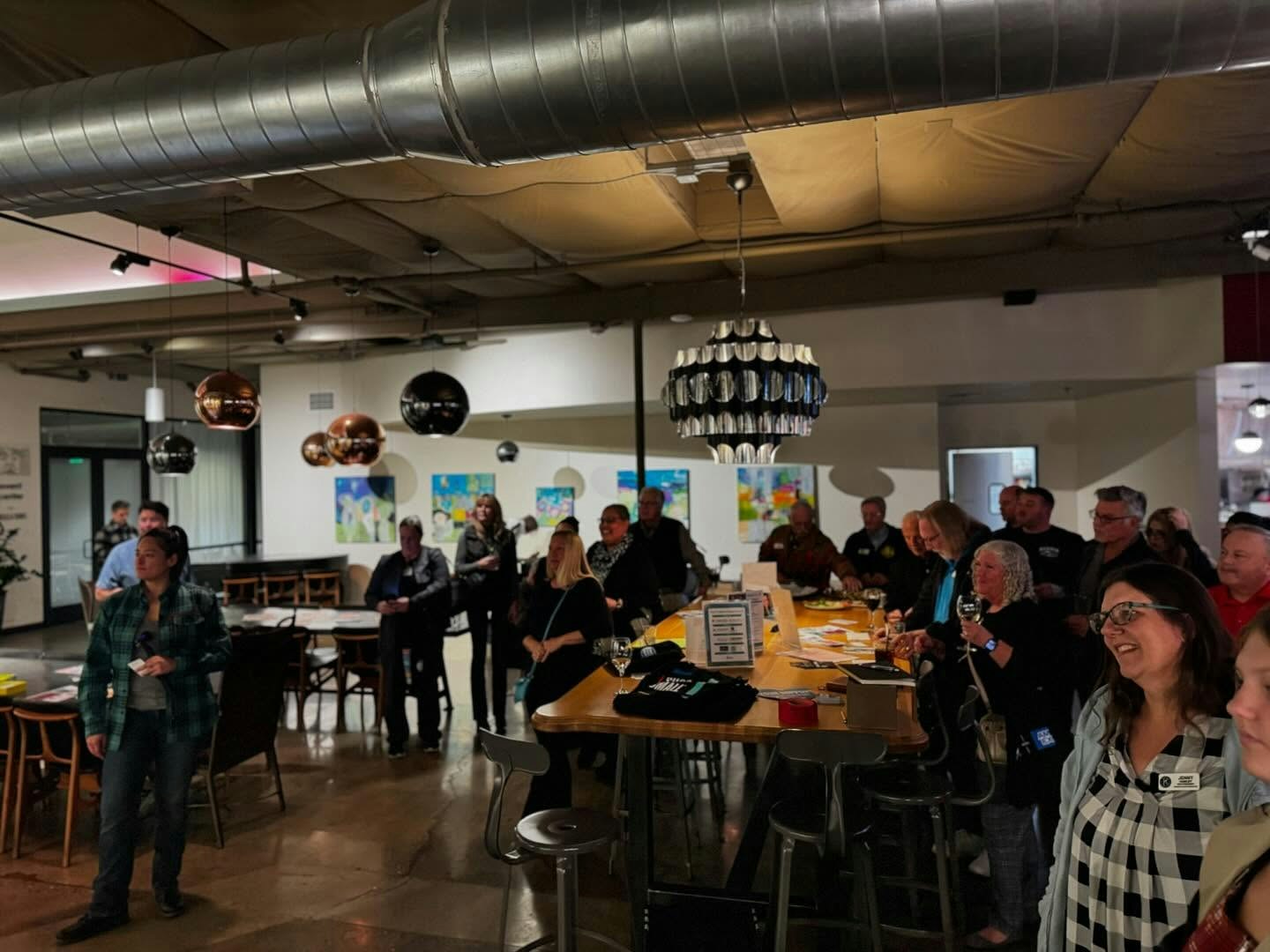 A group of people gathered in a cafe or bar with modern decor, some holding drinks.