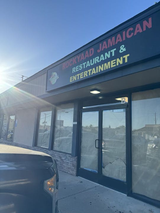 A storefront sign for "Rockyaad Jamaican Restaurant & Entertainment" with sunlight in the corner.