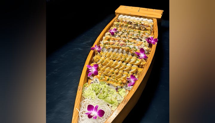 A wooden sushi boat with assorted sushi rolls and purple flowers for garnish.