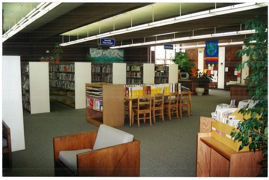 A library interior with bookshelves, a table with chairs, and a sign for "Juvenile Non-Fiction."