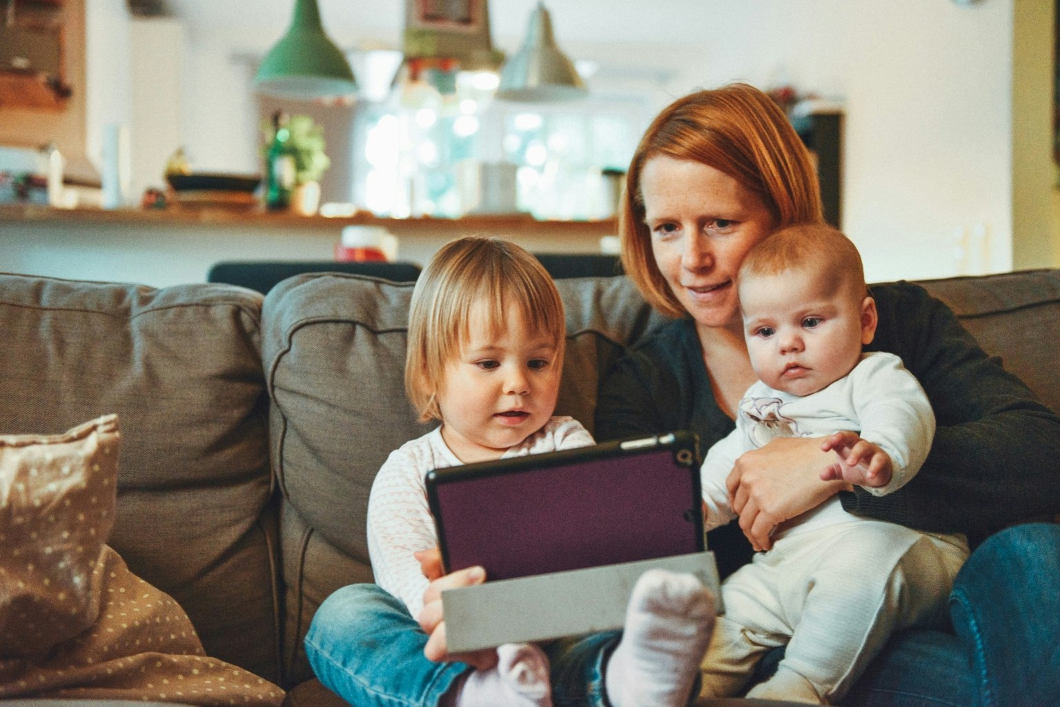A woman with two children sitting on a couch looking at a tablet.