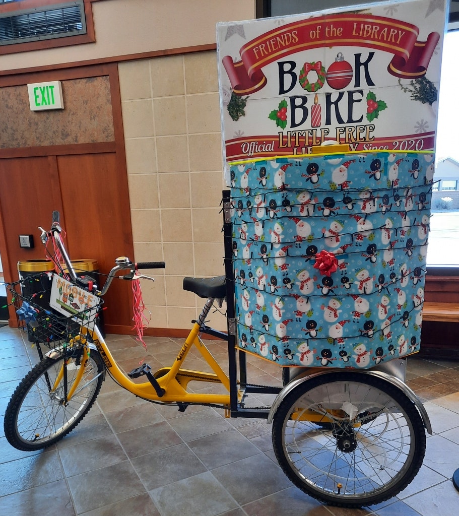 A decorated tricycle with "Book Bike" sign, wrapped in festive paper, inside a building.