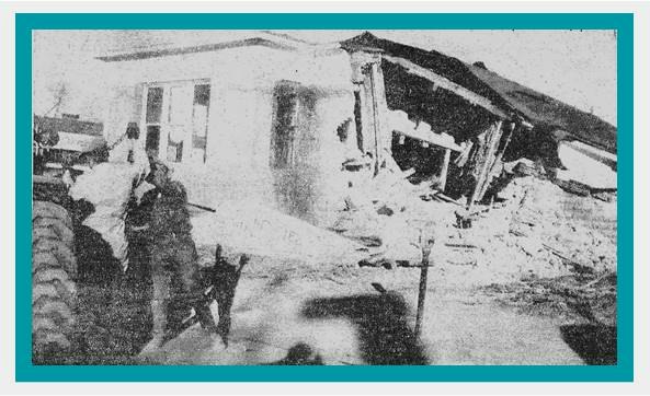 The image shows a damaged building, possibly from an earthquake or disaster, with a person and a dog standing nearby.