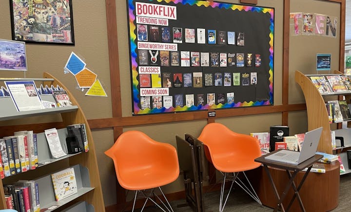 Library teen section with a "BookFlix" board, new books display, orange chairs, and a laptop on a table.