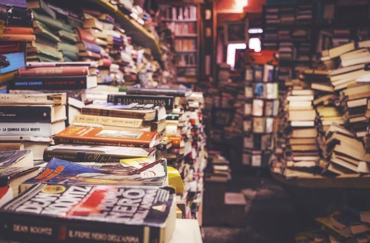 A cluttered, cozy bookstore filled with stacks of books reaching up to the ceiling.